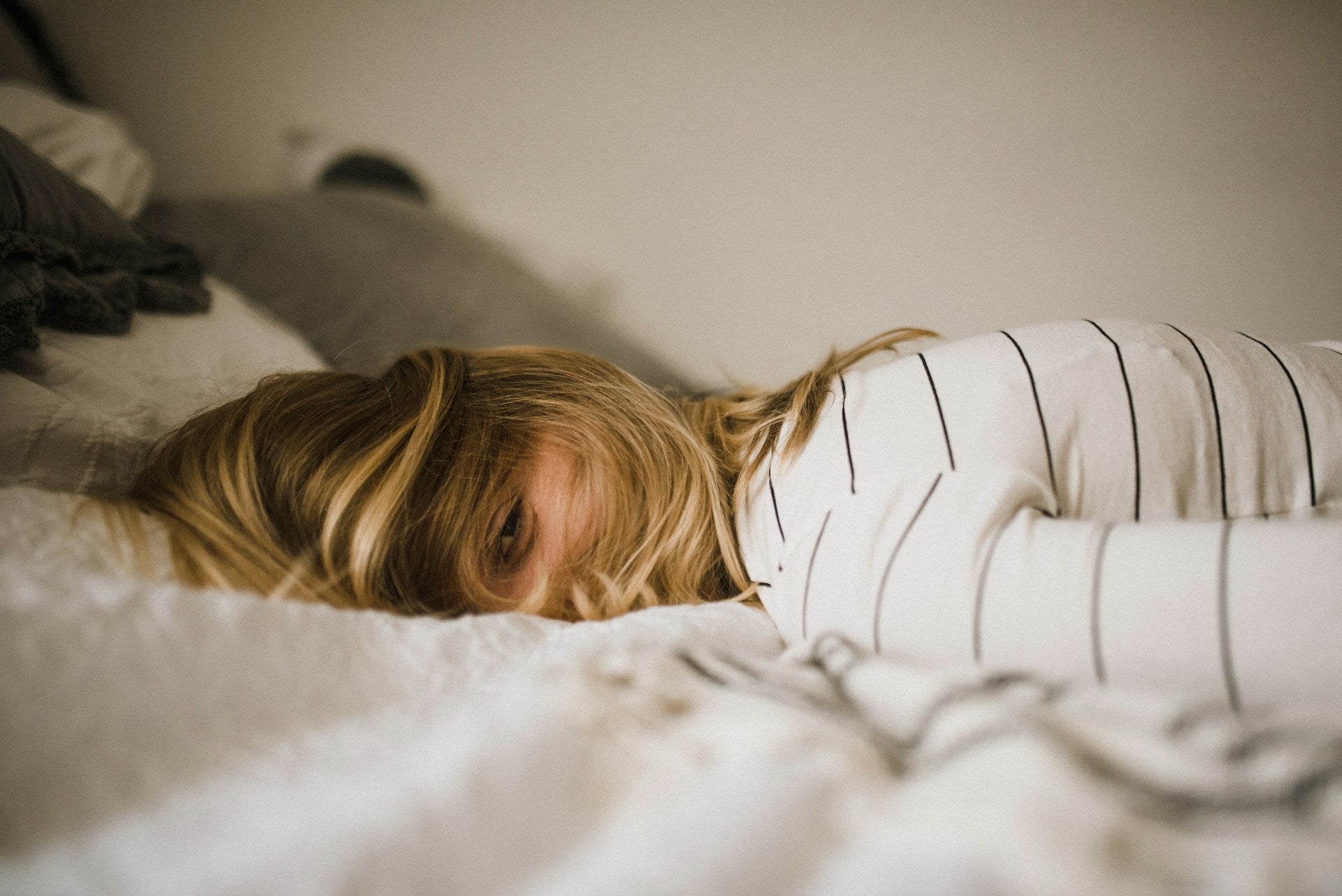Woman lying in bed with hair over face, exhausted and disconnected