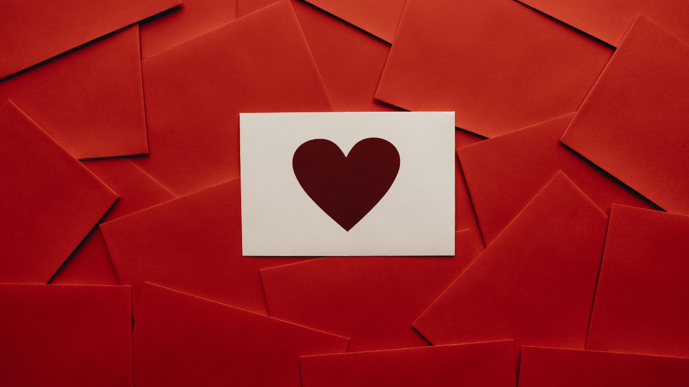 White card with a red heart symbol placed on top of a scattered background of red envelopes, creating a simple Valentine’s‑style love image.