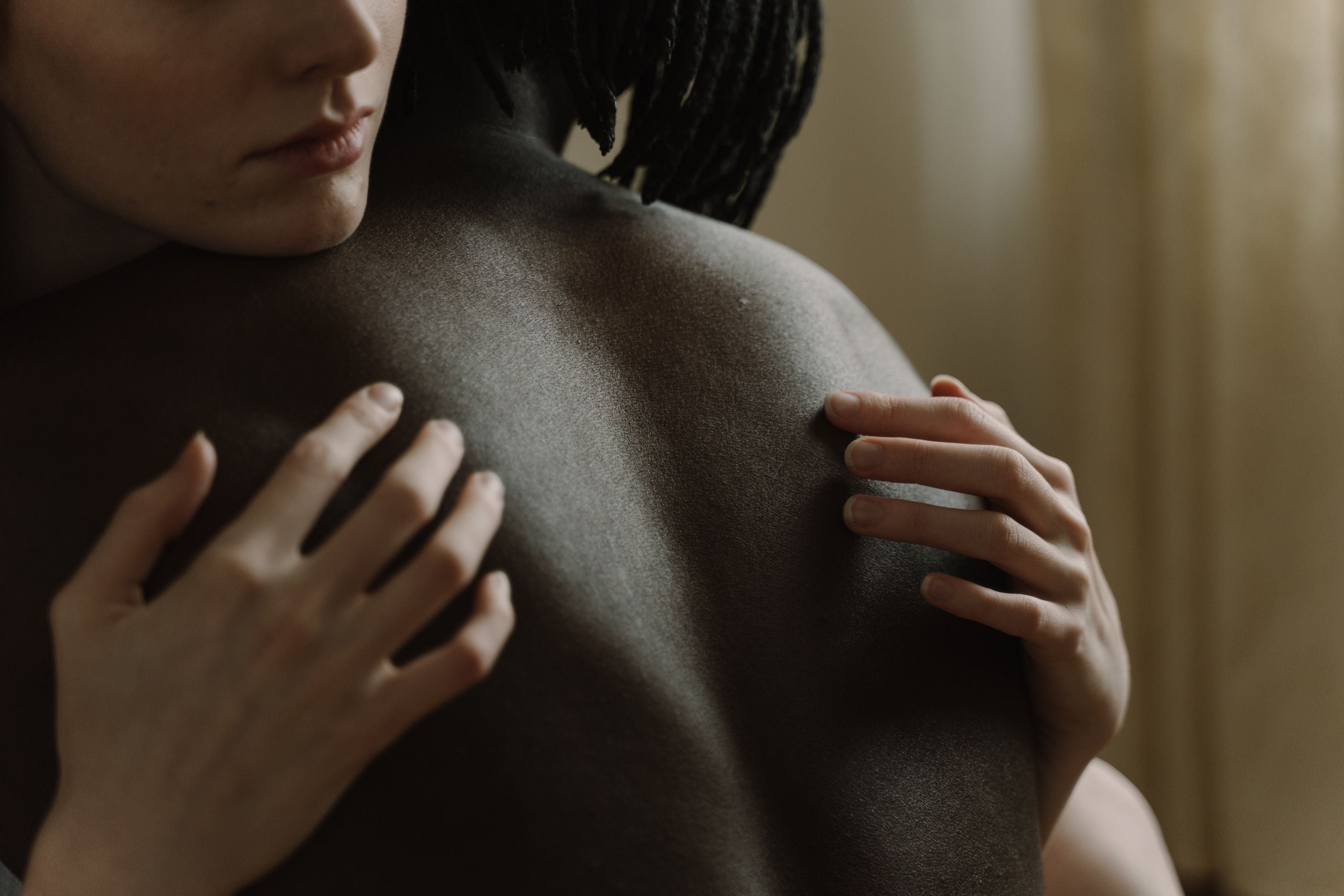 Two partners in a close embrace, hands resting attentively on bare skin, evoking the couples sensory mapping exercise